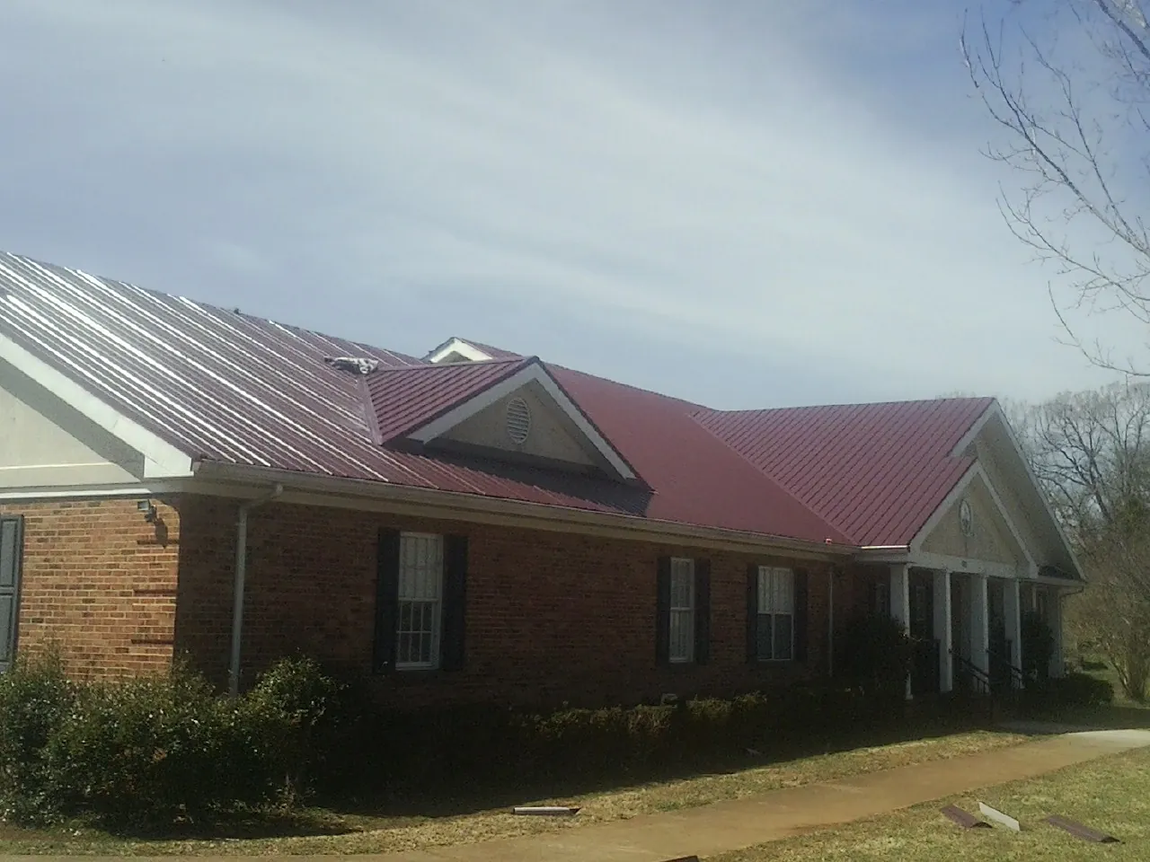 Red metal roof with gabled entries on a long brick building, from a Hail Damage Roof Repair job in Inman