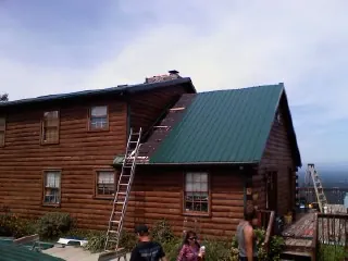 Green metal roof going on a two story log home with ladders set in Inman