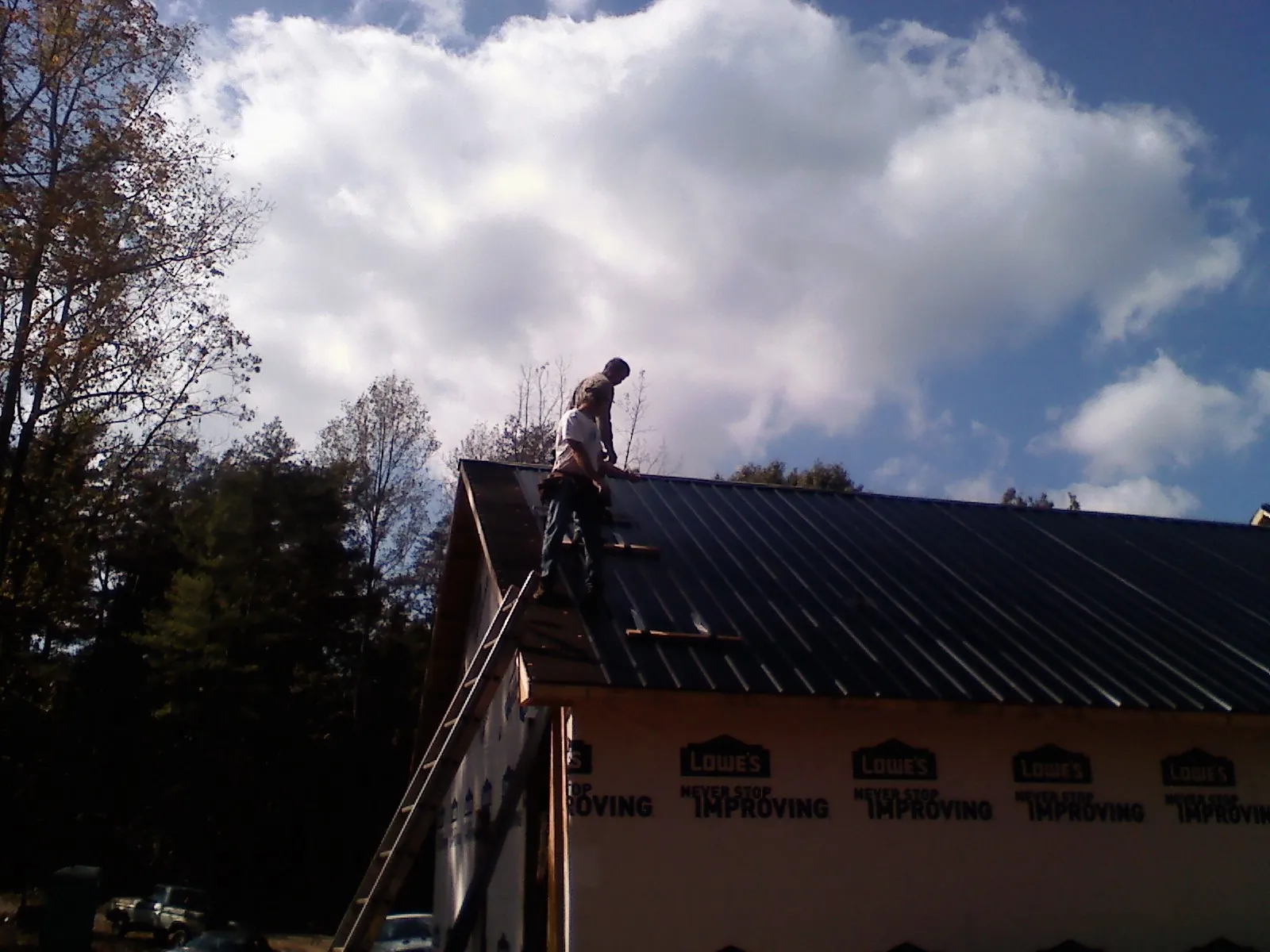 Roofer fastening dark metal panels high against a cloudy sky, from a Roof Inspection job in Inman